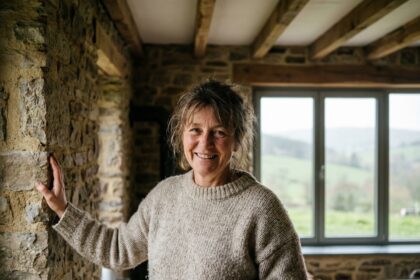 Femme souriante dans une maison en Ardennes touchant un mur en pierre