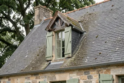 Façade d'une maison régionale française avec lucarne chien-assis en ardoise et volets en bois peints en vert sauge